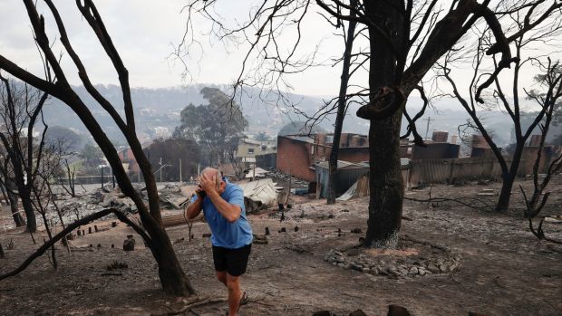 Tathra resident John Plumb on the mobile phone with his neighbours after viewing the aftermath of the bushfire.